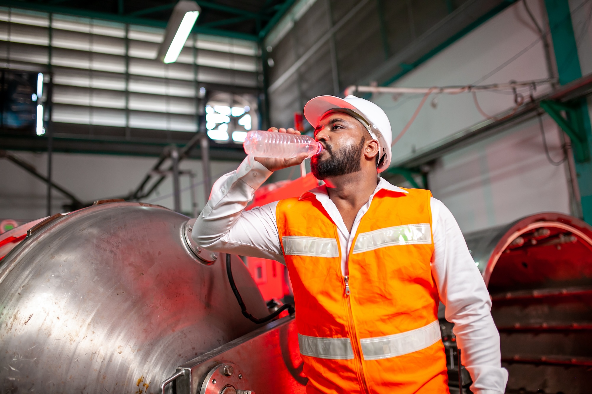 Professional engineers with helmets work to maintain industrial construction equipment. The worker is thirsty and drink refreshing water.